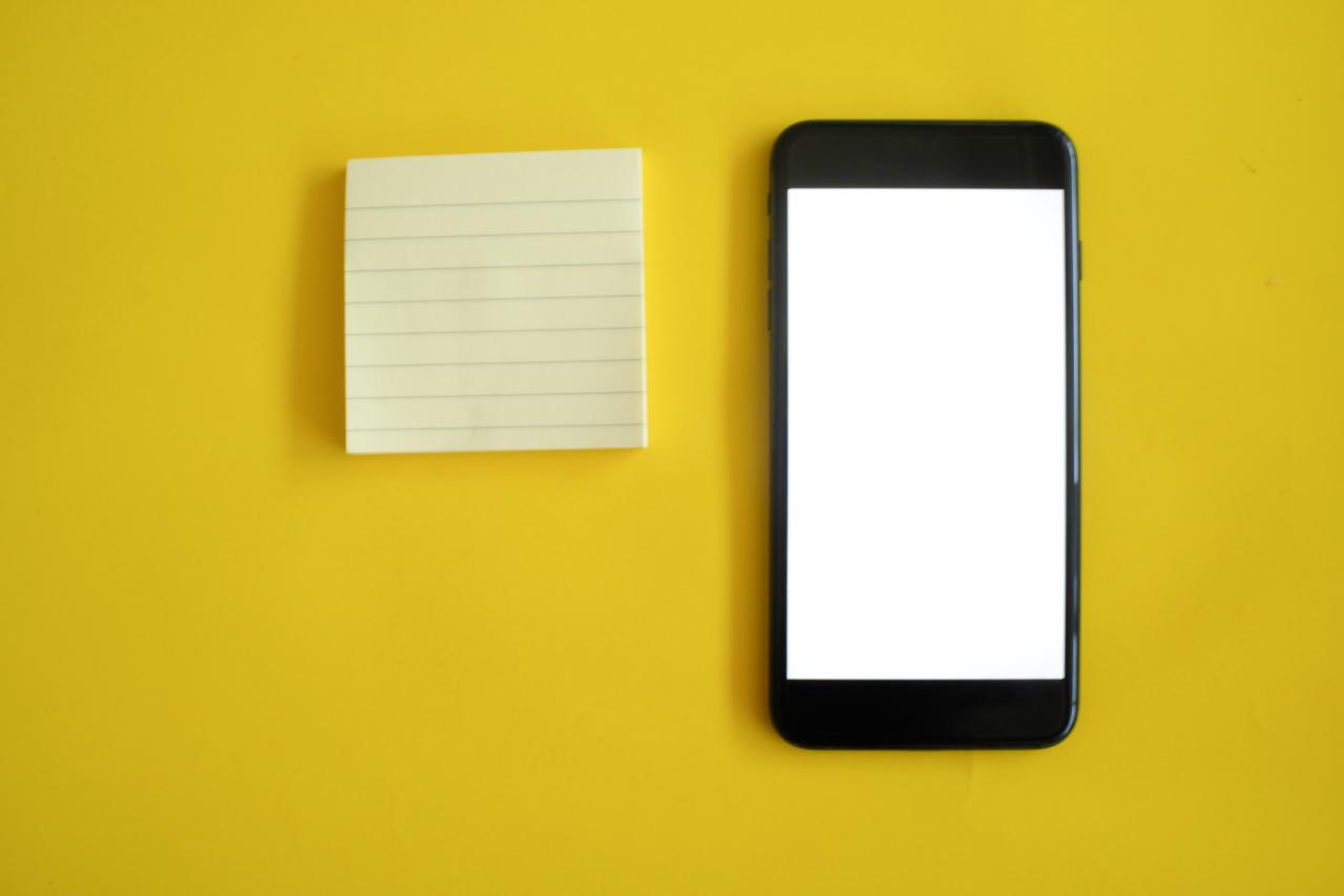 Picture of a smartphone resting on a yellow surface with a small notepad beside it.